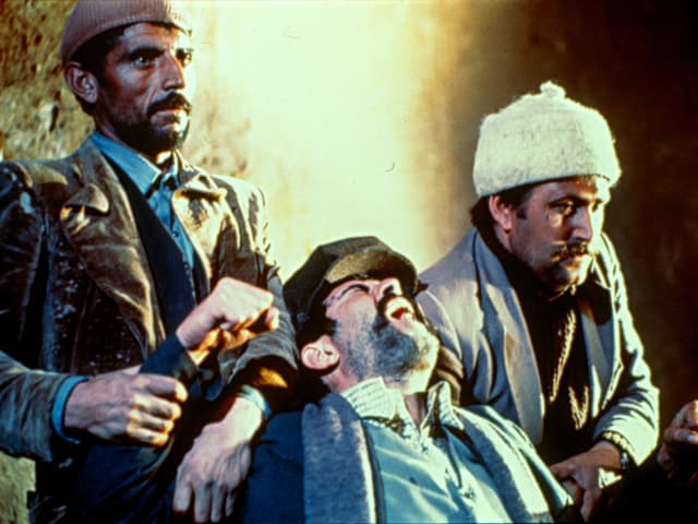 Filmstill: Zwei Männer halten ein Mann, der sich verzweifelt wehrt. Filmstill: Zwei Männer halten ein Mann, der sich verzweifelt wehrt.