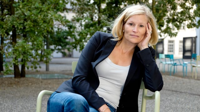 Blonde Frau mit blauem Jackett sitzt auf Stuhl Blonde Frau mit blauem Jackett sitzt auf Stuhl