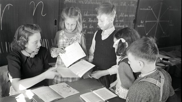 eine schwarz-weiss Fotografie einer Lehrerin, die ihren Schülern etwas am Pult zeigt eine schwarz-weiss Fotografie einer Lehrerin, die ihren Schülern etwas am Pult zeigt