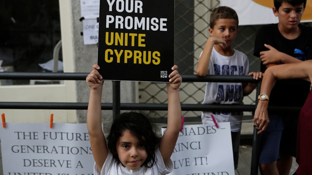 Ein Mädchen hält ein Schild hoch, auf dem "Unite Cyprus" steht. Ein Mädchen hält ein Schild hoch, auf dem "Unite Cyprus" steht.