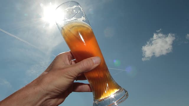Eine Hand hält ein Glas Weissbier gegen die Sonne Eine Hand hält ein Glas Weissbier gegen die Sonne