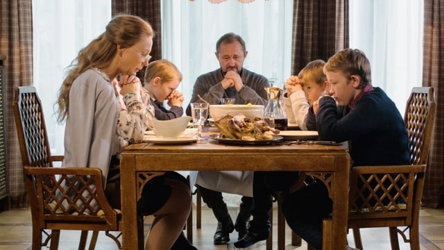 Eine Familie sitzt mit Händen zum Gebet gefaltet um den Esstisch. Eine Familie sitzt mit Händen zum Gebet gefaltet um den Esstisch.
