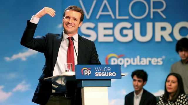 Pablo Casado spricht an einer Wahlkampfverantsaltung. Er trägt einen schwarzen Blazer, rote Krawatte und hebt die rechte Hand. Pablo Casado spricht an einer Wahlkampfverantsaltung. Er trägt einen schwarzen Blazer, rote Krawatte und hebt die rechte Hand.