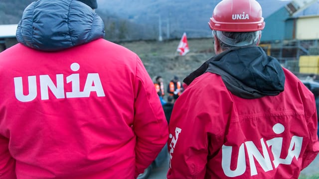 Zwei Männer in roten Jachen der Gewerkschaft Unia von hinten fotogografiert Zwei Männer in roten Jachen der Gewerkschaft Unia von hinten fotogografiert