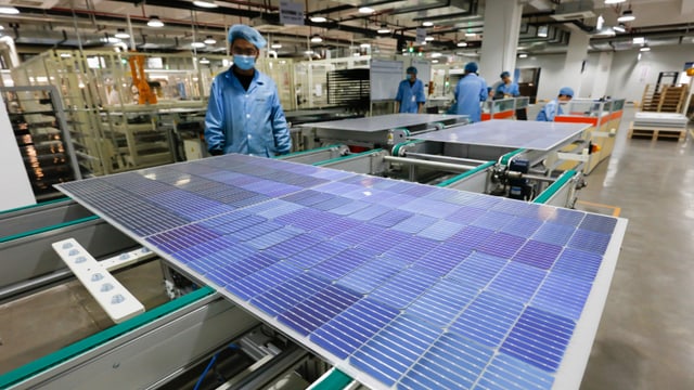Arbeiter in chinesischer Firma steht vor Solarpanel Arbeiter in chinesischer Firma steht vor Solarpanel