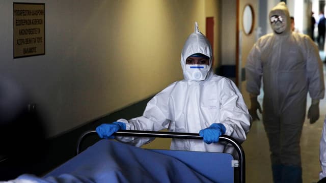 Krankenhauspersonal in Schutzkleidung schiebt ein Bett durch den Gang. Krankenhauspersonal in Schutzkleidung schiebt ein Bett durch den Gang.