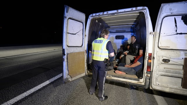 Ein Polizist steht vor einem Lieferwagen mit Migranten drin. Ein Polizist steht vor einem Lieferwagen mit Migranten drin.