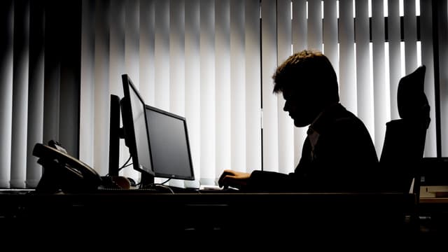Symbolbild: Mann im Gegenlicht vor einem Computer. Symbolbild: Mann im Gegenlicht vor einem Computer.