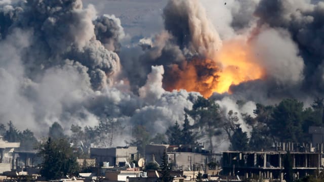 Eine Explosion und Rauch steigen über Häusern auf Eine Explosion und Rauch steigen über Häusern auf