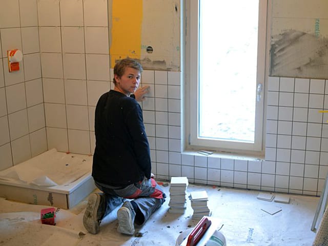 Ein Plattenleger auf den Knien fixiert weisse Plättli in der neuen grossen Dusche in der Hörnlihütte.