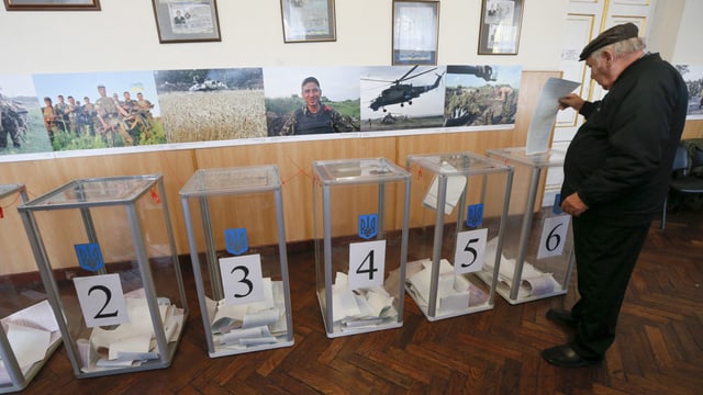 Ein älterer Mann legt seinen Stimmzettel in eine gläserne Wahlurne ein. Ein älterer Mann legt seinen Stimmzettel in eine gläserne Wahlurne ein.