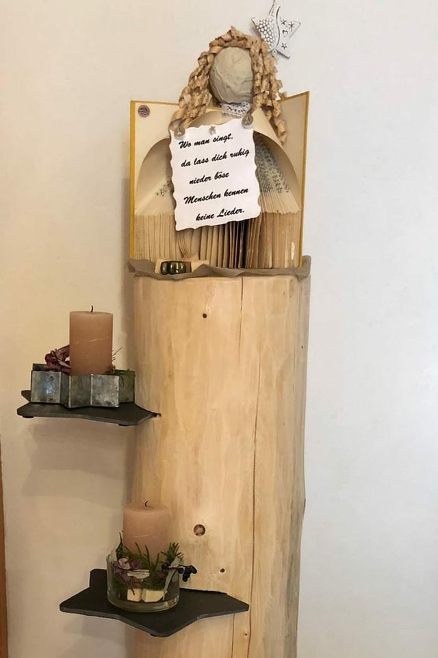 Holzstamm mit Etagen auf denen vier Kerzen stehen und zuoberst ein Engel mit weisem Spruch in der Hand: "Wo Man singt, da lass dich ruhig nieder. Böse Menschen kennen keine Lieder.