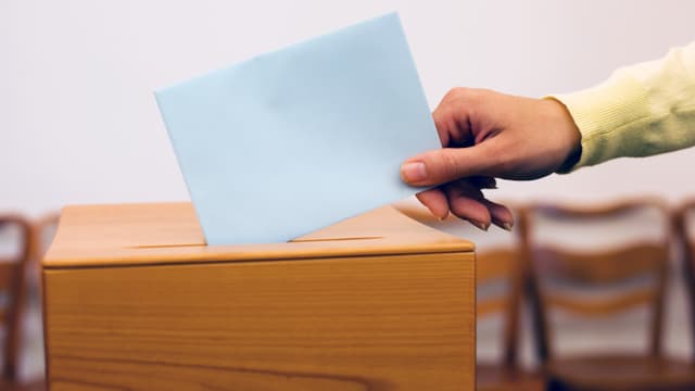 Hand hält Couvert über Urne. Hand hält Couvert über Urne.