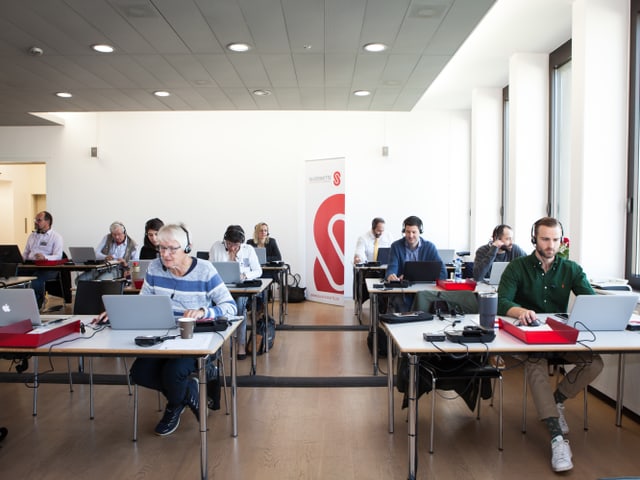 Viele Menschen im Büro mit Kopfhörern.
