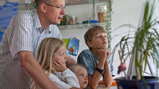 Vater sitzt mit drei Kindern vor Computer. Symbolbild für den Erfolg von Familienunternehmen. Vater sitzt mit drei Kindern vor Computer. Symbolbild für den Erfolg von Familienunternehmen.