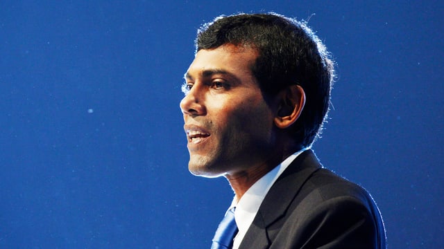 Nasheed in hellem Scheinwerferlicht vor einer blauen Wand.