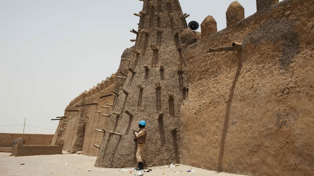 UNO-Blauhelm steht vor einem Sandsteingebäude. UNO-Blauhelm steht vor einem Sandsteingebäude.