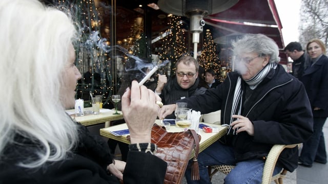 Drei Personen sitzen an einem Tischchen draussen und rauchen. Im Hintergrund ist ein Heizpilz.