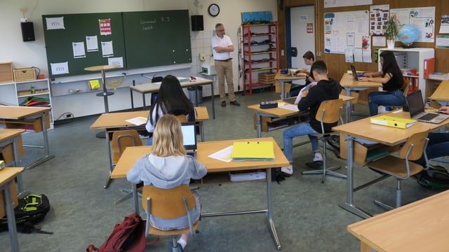 Schülerinnen und Schüler sitzen an Einzelpulten. Vorne steht Lehrer Franz Gehrig. Schülerinnen und Schüler sitzen an Einzelpulten. Vorne steht Lehrer Franz Gehrig.