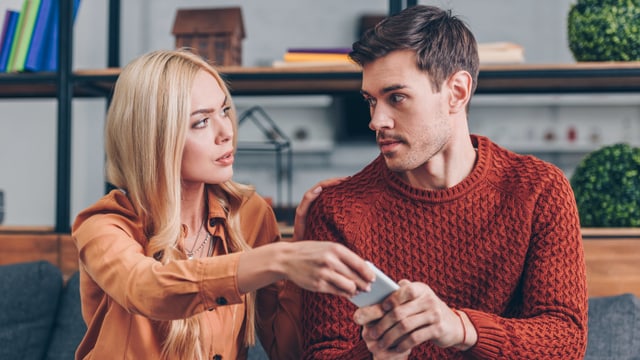 Eine Frau nimmt dem Mann sein Handy aus der Hand. Eine Frau nimmt dem Mann sein Handy aus der Hand.