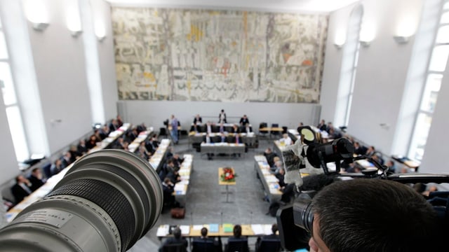Ein Fotograf und ein Kameramann nehmen eine Debatte im Grossen Rat auf, von der Tribüne aus. Ein Fotograf und ein Kameramann nehmen eine Debatte im Grossen Rat auf, von der Tribüne aus.