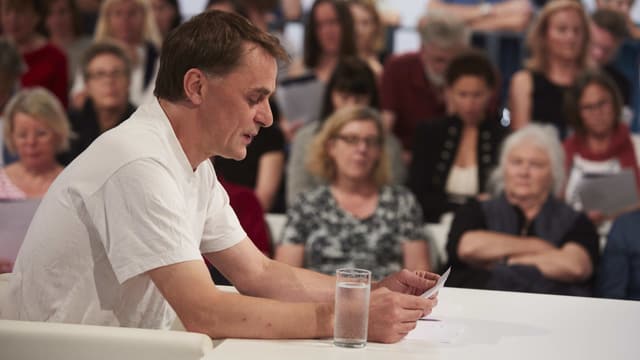 Ein Mann in weissem Shirt liest an einem tisch von einem Blatt. Ein Mann in weissem Shirt liest an einem tisch von einem Blatt.