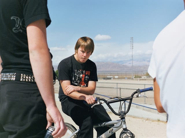 Ein Junge auf einem BMX, neben ihm stehen zwei andere Menschen.