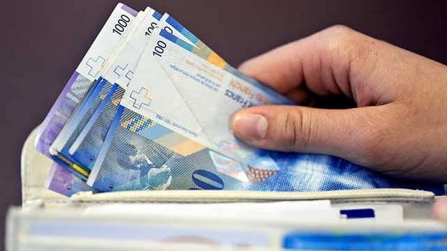 Eine Hand hält mehrere Banknoten, die aus einem Portemonnaie hervorragen. Eine Hand hält mehrere Banknoten, die aus einem Portemonnaie hervorragen.