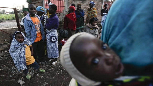 Schwarze Menschen auf der Flucht, im Vorderund ein Baby, das mit grossen Augen in die Kamera blickt. Schwarze Menschen auf der Flucht, im Vorderund ein Baby, das mit grossen Augen in die Kamera blickt.