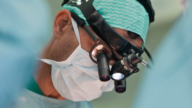 Operierender Arzt mit Lupenbrille Operierender Arzt mit Lupenbrille