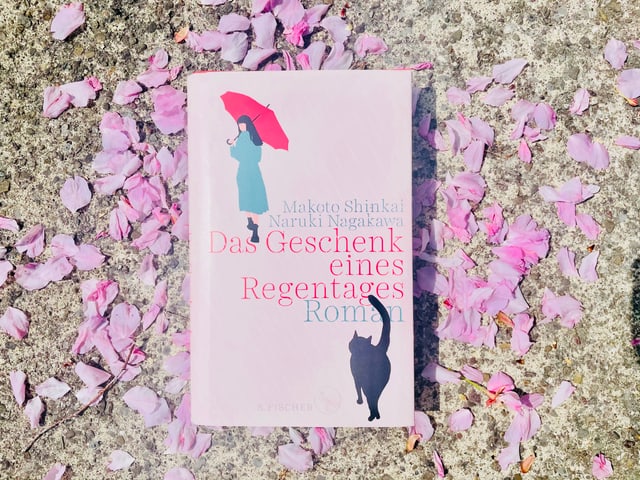 Der Roman «Das Geschenk eines Regentages» von Makoto Shinkai und Naruki Nagakawa liegt auf Kirschblüten Der Roman «Das Geschenk eines Regentages» von Makoto Shinkai und Naruki Nagakawa liegt auf Kirschblüten