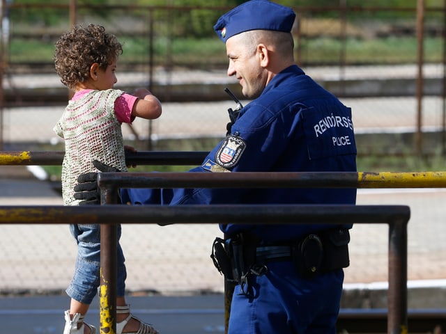 Ein ungarischer Polizist spielt an einem Bahnhof mit einem Flüchtlingsmädchen