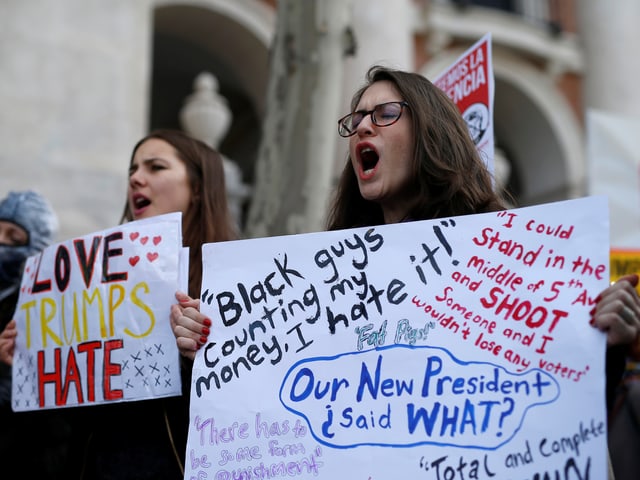 Zwei Frauen halten Anti-Trump-Schilder und rufen etwas.