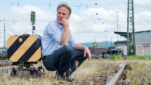 Ein älterer Herr kauert am Boden vor ausrangierten Bahngleisen. Ein älterer Herr kauert am Boden vor ausrangierten Bahngleisen.