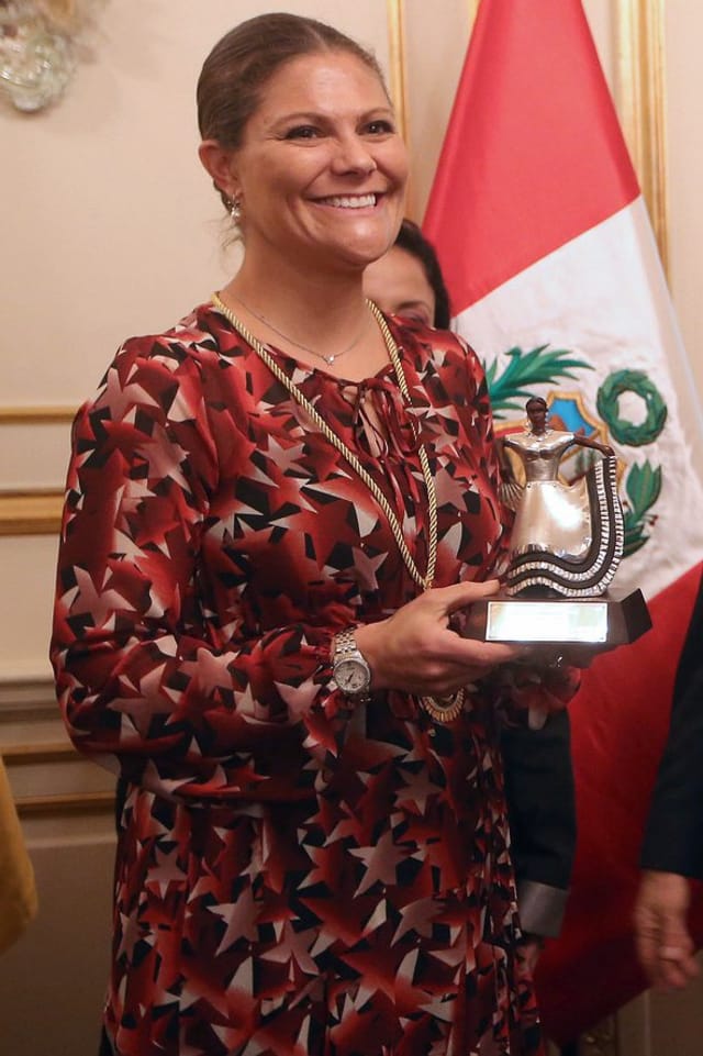 Victoria in einem dunkelroten Kleid, lachend und eine Puppe in der Hand haltend. Victoria in einem dunkelroten Kleid, lachend und eine Puppe in der Hand haltend.
