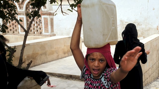 Kind transportiert Wasserberhälter auf dem Kopf