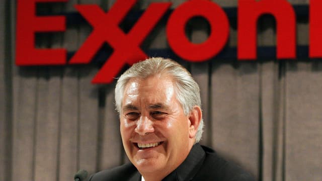Rex Tillerson lacht in die Kamera vor dem roten Logo von ExxonMobil Rex Tillerson lacht in die Kamera vor dem roten Logo von ExxonMobil
