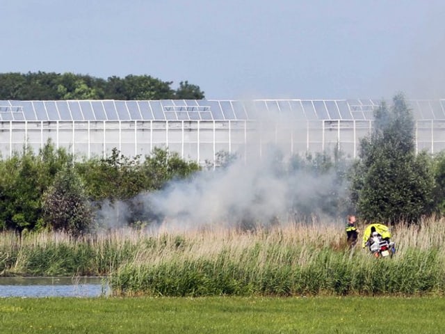Der rauchende Absturzort in einem Teich. Im Hintergrund ein riesiges Gewächshaus.