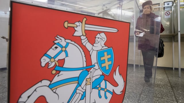 Frau in einer Wahlkabine in Vilnius, davor Wappen von Litauen. 