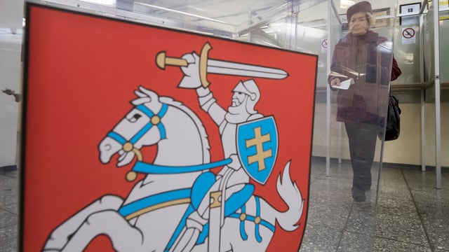Frau in einer Wahlkabine in Vilnius, davor Wappen von Litauen. Frau in einer Wahlkabine in Vilnius, davor Wappen von Litauen.