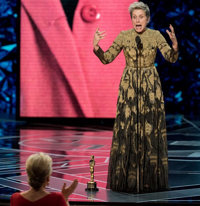 Frau in langem goldenen Kleid freut sich auf der bühne über den Oscar. Frau in langem goldenen Kleid freut sich auf der bühne über den Oscar.