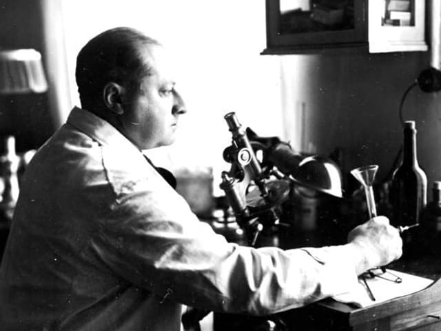 Gottfried Benn im Arztkittel, sitzend vor einem Mikroskop. Gottfried Benn im Arztkittel, sitzend vor einem Mikroskop.
