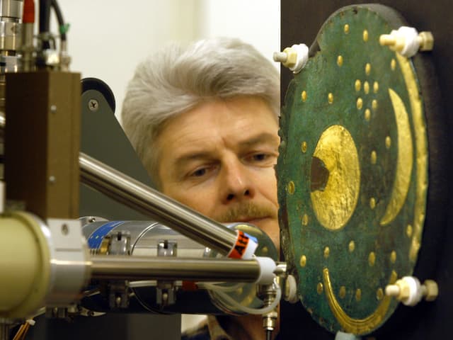 Ein Mann beobachtet eine Maschine, die auf die Himmelsscheibe von Nebra gerichtet ist Ein Mann beobachtet eine Maschine, die auf die Himmelsscheibe von Nebra gerichtet ist