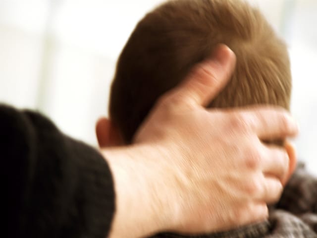 Hand greift an den Hinterkopf eines Jungen.