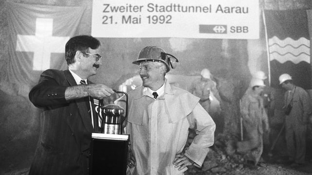 Zwei Männer stehen in einem Tunnel, dahinter stehen Bahnarbeiter zu herum. Zwei Männer stehen in einem Tunnel, dahinter stehen Bahnarbeiter zu herum.
