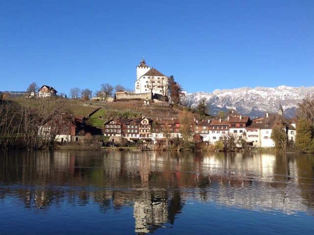 EIn schönes Schloss, ein See im Vordergrund, blauer Himmel.