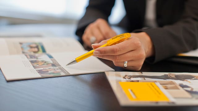 Eine Frau hält einen Postfinance-Kugelschreiber und zeigt etwas in einer Broschüre. Eine Frau hält einen Postfinance-Kugelschreiber und zeigt etwas in einer Broschüre.