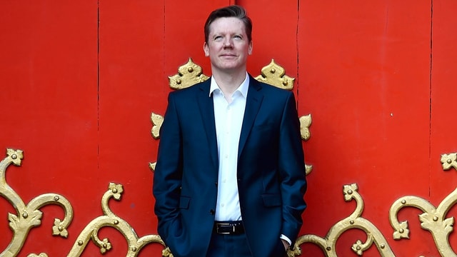 Fergus Linehan steht vor einer roten Wand. Fergus Linehan steht vor einer roten Wand.