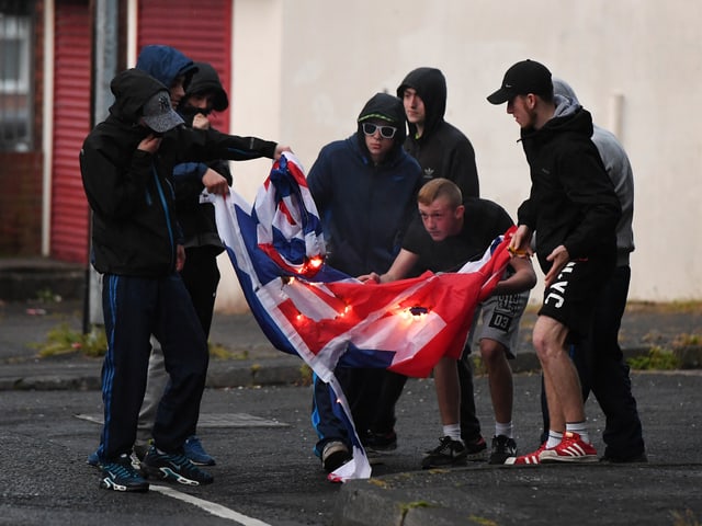 Schwarz gekleidete Jugendliche verbrennen auf der Strasse eine Union Jack-Flagge. Schwarz gekleidete Jugendliche verbrennen auf der Strasse eine Union Jack-Flagge.