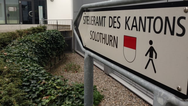 Wegweiser zum Steueramt des Kantons mit dem Kantonswappen und einem Piktogramm eines Mannes daarauf. Wegweiser zum Steueramt des Kantons mit dem Kantonswappen und einem Piktogramm eines Mannes daarauf.